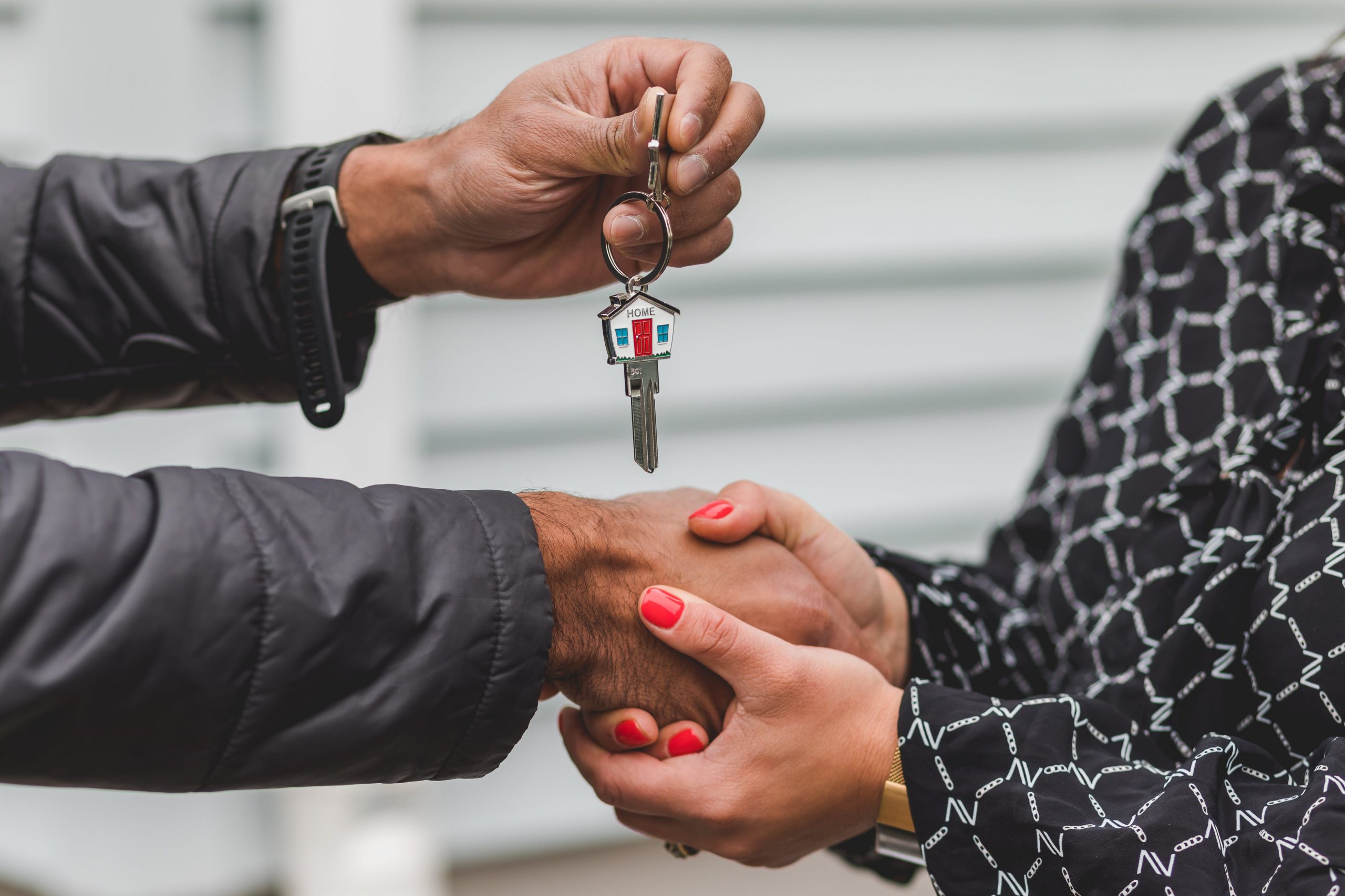 two people shaking hands while passing keys labeled Home Sweet Home from realtor to buyer